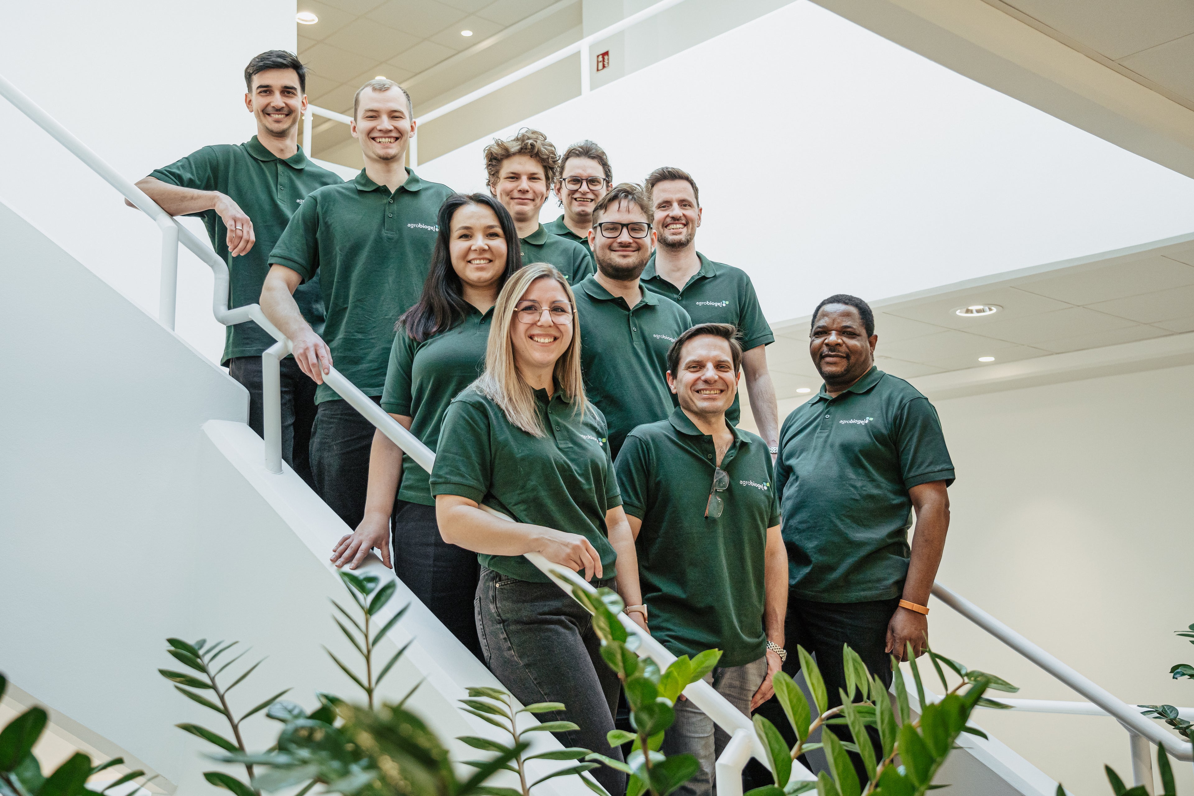 Team von Agrobiogel, bestehend aus zehn Personen in grünen Polohemden mit Firmenlogo, stehend auf einer Treppe in einem modernen Bürogebäude.