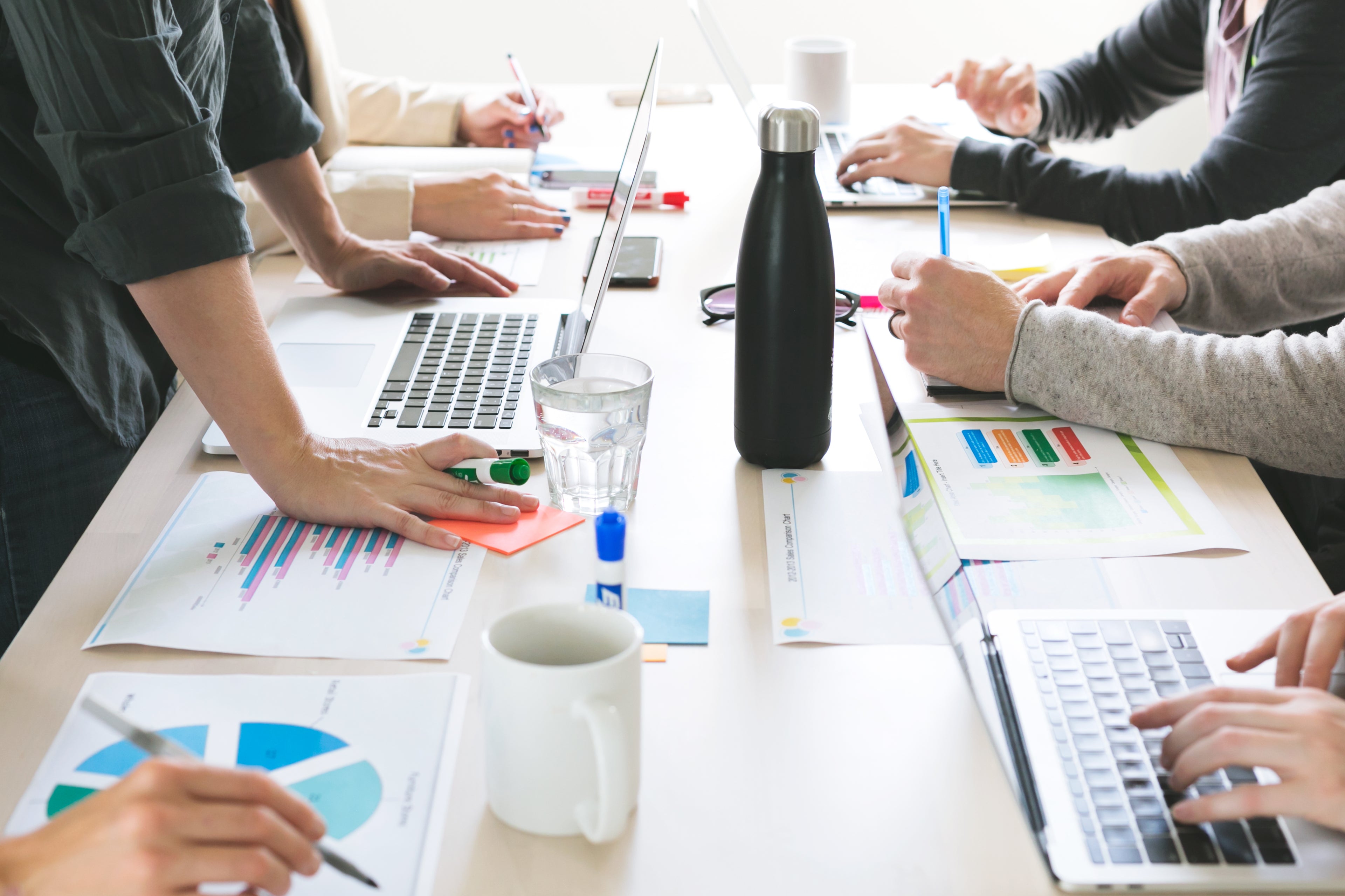 Im Büro sitzen Personen mit Laptops, Zetteln, Trinkflasche und Kaffee und arbeiten an einer Strategie